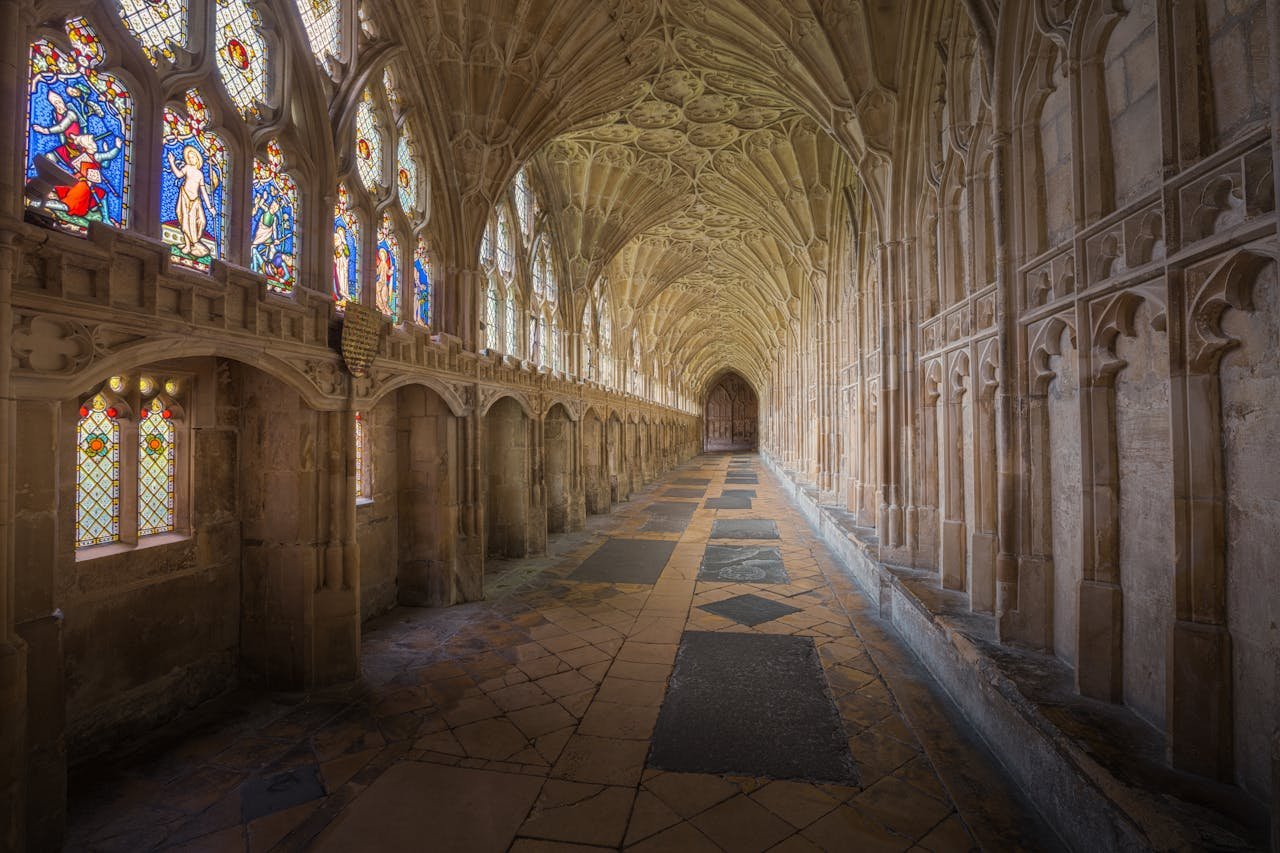 Gothic cloisters of Gloucester Cathedral showcasing intricate arches and vibrant stained glass windows.